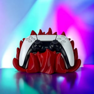 May include: A white video game controller sits in a red, flame-shaped stand. The controller has black buttons and triggers.
