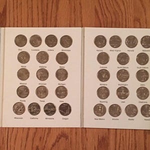 May include: A white album with a black spine containing a collection of 50 state quarters. The album is open to reveal the coins, which are arranged in rows and columns. The album also includes a list of the states and their corresponding quarters.