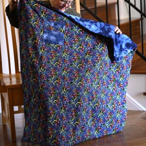 May include: A person holding a blue and multi-colored quilt with a blue pocket. The quilt has a swirling pattern.