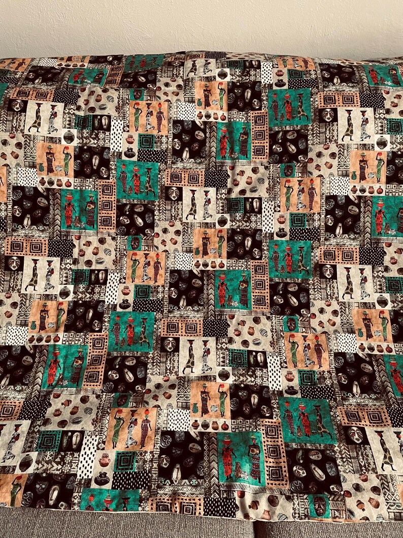 May include: A colorful fabric with a repeating pattern of African women carrying pots on their heads. The fabric is a patchwork of different colors and patterns, including black, white, brown, green, and orange.