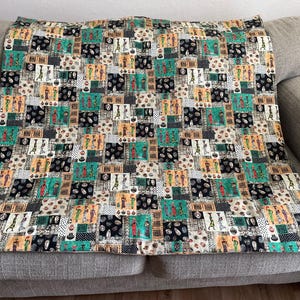 May include: A colorful throw blanket with a repeating pattern of stylized figures in black, white, green, and brown. The figures are set against a background of geometric shapes.