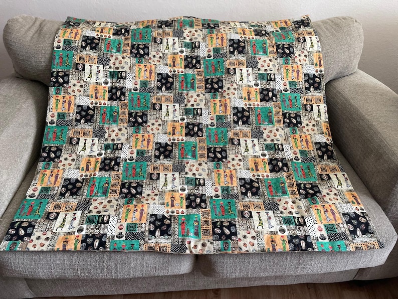 May include: A colorful throw blanket with a repeating pattern of stylized figures in black, white, green, and brown. The figures are set against a background of geometric shapes.
