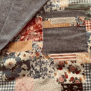 Puede incluir: Una colcha de retazos con una variedad de patrones florales en tonos de azul, rojo y blanco. La colcha est&aacute; hecha de diferentes telas, incluyendo denim, algod&oacute;n y lino.