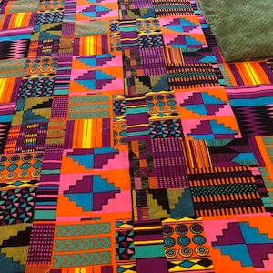 May include: A vibrant patchwork textile featuring a geometric pattern in shades of orange, purple, pink, teal, and black. The fabric is likely cotton or a similar material, with a repeating design of squares and rectangles. The overall aesthetic is bold and colorful.