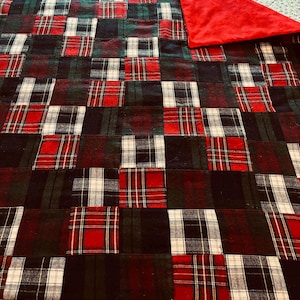 May include: A patchwork quilt featuring a plaid pattern in red, green, black, and white. The quilt has a solid red backing. The plaid squares are arranged in a grid pattern, creating a cozy and rustic aesthetic.