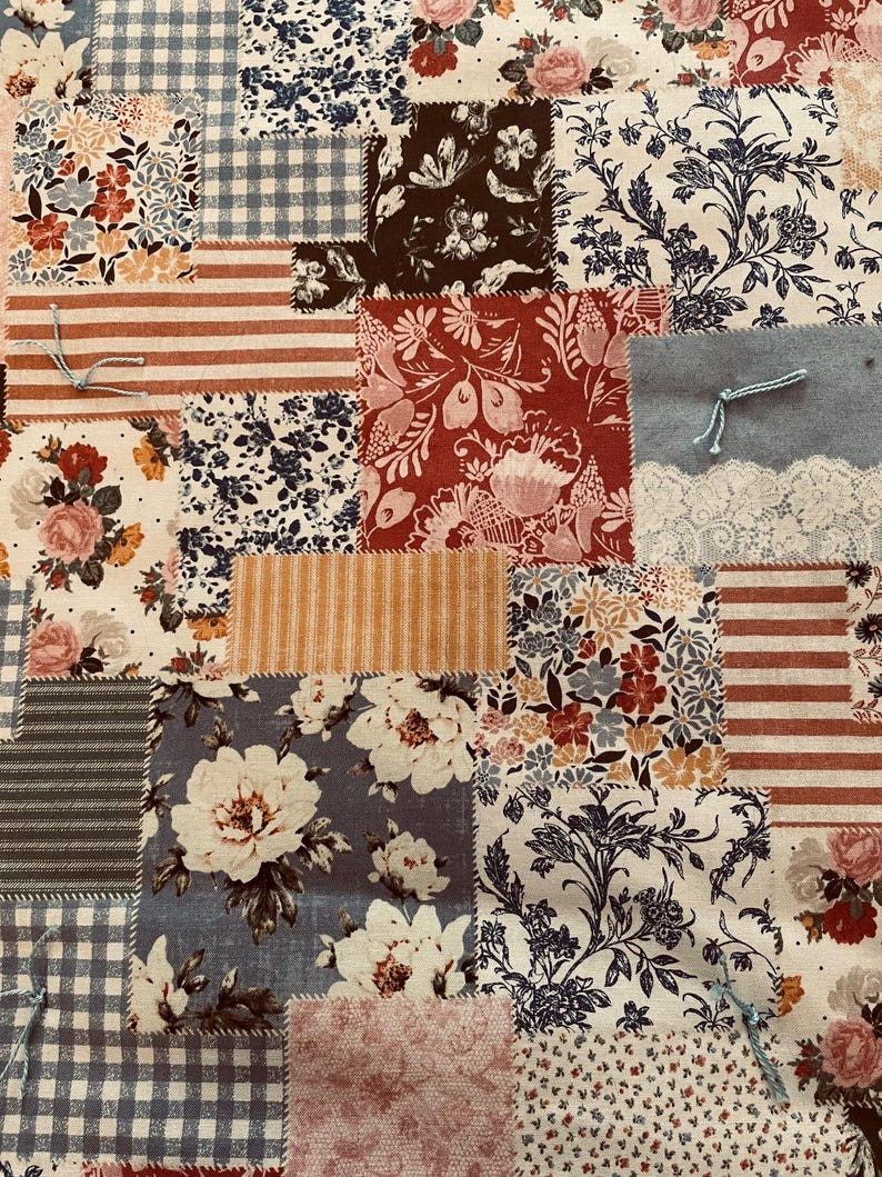 Puede incluir: Una tela de patchwork con una variedad de patrones florales en tonos de azul, rojo y blanco. La tela est&aacute; compuesta por cuadrados y rect&aacute;ngulos, y las costuras son visibles.