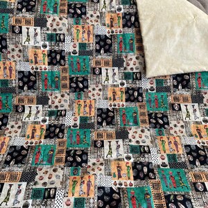 May include: A patchwork quilt featuring a repeating pattern of African women carrying pots on their heads. The quilt is made of a variety of fabrics in shades of brown, black, green, and white. The background is a cream-colored fabric.