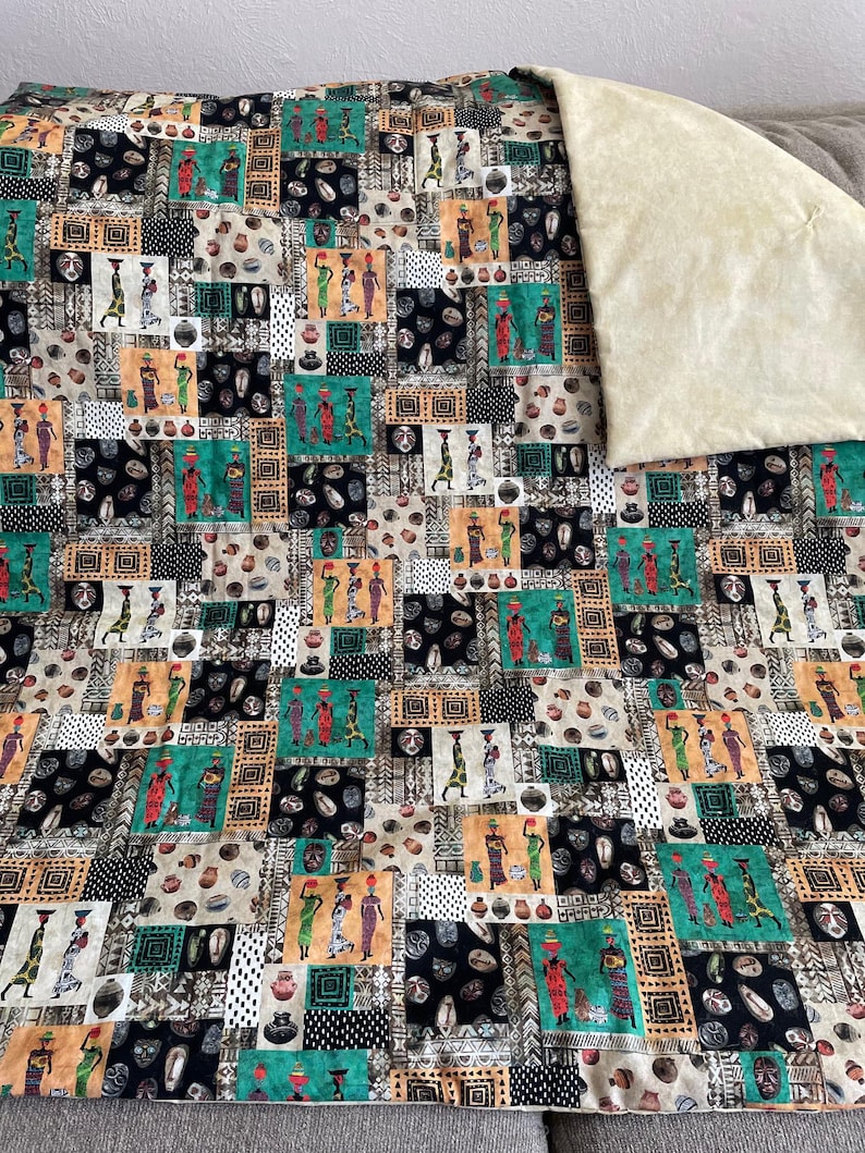 May include: A patchwork quilt featuring a repeating pattern of African women carrying pots on their heads. The quilt is made of a variety of fabrics in shades of brown, black, green, and white. The background is a cream-colored fabric.