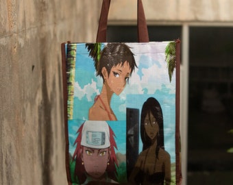 May include: A brown tote bag with a colourful design featuring three anime characters. The characters are a woman with long brown hair, a woman with short brown hair, and a man with red hair wearing a hat.