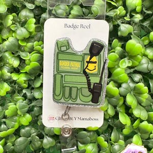 May include: Green and black badge reel with a glitter border patrol vest design. The vest has the words "Border Patrol Federal Agent" on it. The badge reel has a silver clip.