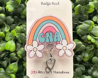 May include: A glittery badge reel on a display card labeled Badge Reel and Glitter Buy Mamaboss. The reel features a rainbow graphic with the text CNA in the center, flanked by two white flowers with light pink centers on each side.