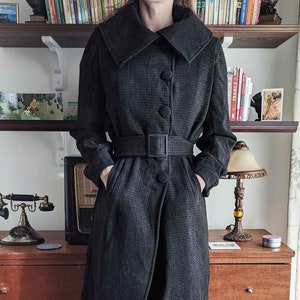 Könnte beinhalten: Ein schwarz-weiß karierter Wollmantel mit großem Kragen und Gürtel. Der Mantel hat einen einzigen Knopfverschluss und Taschen an der Vorderseite.
