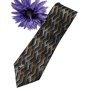 May include: A patterned tie with a repeating chevron design in black, brown, and gold. The tie features a small emblem near the bottom. A purple flower is in the upper left corner.