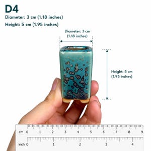 May include: A small square ceramic pot with a teal and dark blue speckled glaze. The pot is labeled D4 and measures 3 cm (1.18 inches) in diameter and 5 cm (1.95 inches) in height, as indicated by the text and ruler visible in the image.