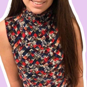 May include: A sleeveless, high-neck top with a geometric pattern of red, navy, and brown diamonds. The fabric has a corduroy texture and is adorned with white floral scrollwork. The top is a vintage style.