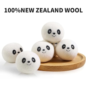 May include: Five white wool dryer balls with panda faces printed on them. The balls are arranged on a wooden tray. 100% New Zealand Wool.