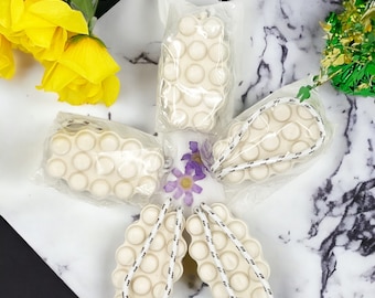 May include: Five white bath poufs with a textured surface and a white rope handle. The poufs are arranged in a star shape on a white marble surface.
