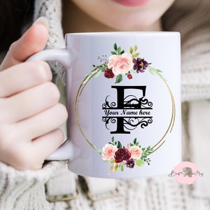 Può includere: Una tazza in ceramica bianca con un bordo dorato e un motivo floreale. Il motivo presenta una grande lettera "F" con una fioritura decorativa e il testo "Your Name here".