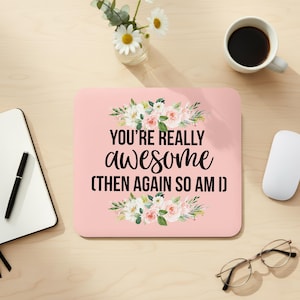 May include: A pink mousepad with the text "YOU'RE REALLY awesome (THEN AGAIN SO AM I)" in black script. Floral arrangements in white, pink, and green adorn the top and bottom. A white mouse, coffee cup, and glasses are also visible.