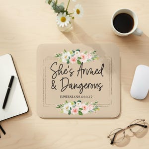 Peut inclure: Tapis de souris beige avec l'inscription "She's Armed & Dangerous" et Éphésiens 6:10-17, orné de motifs floraux. Une souris blanche, une tasse de café et des lunettes sont sur le bureau. Un bloc-notes et un stylo sont également visibles.