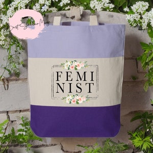 May include: A purple, beige, and white tote bag with the word "FEMINIST" in black lettering surrounded by a floral design.