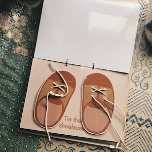 May include: A brown and beige children's book with two brown shoes with white laces. The text on the book says "Tie the shoelaces".