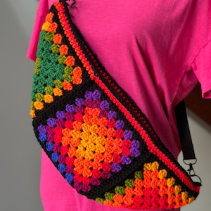 May include: A colorful crocheted crossbody bag with a black strap. The bag is made of granny squares in shades of red, orange, yellow, green, blue, and purple.