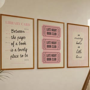 以下が含まれることがあります： 明るい木製フレームに入った3枚の壁掛けアート。左は図書館の貸出カードのデザインで「Between the pages of a book is a lovely place to be」と書かれています。中央は「LATE NIGHT BOOK CLUB」と書かれたピンクのチケット3枚。右はピンクのストライプ柄で「so many books so little time」と書かれています。