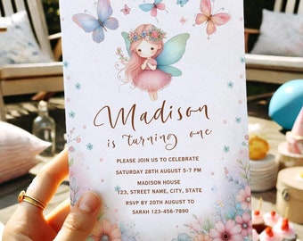 May include: A watercolor invitation card featuring a fairy with pink hair, a floral crown, and butterfly wings. The card reads "Madison is turning one" with event details. Soft pastel colors and floral accents decorate the edges.