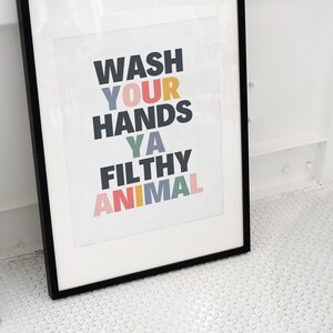 May include: A black framed print with the text "Wash your hands ya filthy animal" in colorful letters.