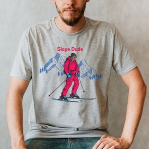 May include: A gray t-shirt with a graphic of a skier in a red and blue ski suit. The graphic says "Slope Dude" above the skier.