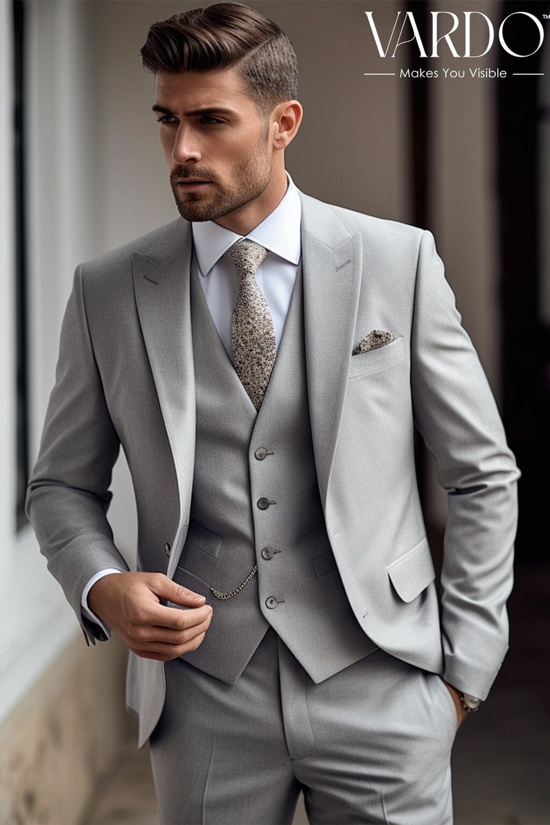 Pu&ograve; includere: Un abito grigio a tre pezzi con una cravatta fantasia e un fazzoletto da taschino. La giacca del vestito ha una chiusura con un solo bottone e una catena da tasca. Il vestito &egrave; realizzato da Vardo, un marchio che ti rende visibile.