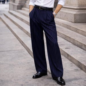 May include: Navy blue pinstripe trousers with a wide leg, paired with black leather dress shoes. The trousers have a high waist and pleats. A black belt and a white dress shirt complete the look. The outfit is suitable for formal occasions.