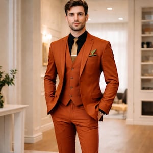 Könnte beinhalten: Ein dreiteiliger Anzug in Rostfarbe mit einem schwarzen Hemd und einer goldenen Krawatte. Der Anzug besteht aus einem Blazer, einer Weste und einer Hose. Ein kleiner grüner Akzent befindet sich in der Blazer-Tasche. Der Anzug ist maßgeschneidert und scheint aus einem glatten Stoff zu sein.