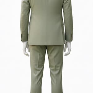 K&ouml;nnte beinhalten: Ein hellgr&uuml;ner Anzug, bestehend aus Blazer und Hose, pr&auml;sentiert auf einer Schaufensterpuppe. Der Blazer hat zwei Kn&ouml;pfe an jeder Manschette. Der Anzug ist einfarbig und scheint aus einem glatten Stoff zu sein. Braune Lederschuhe sind sichtbar.