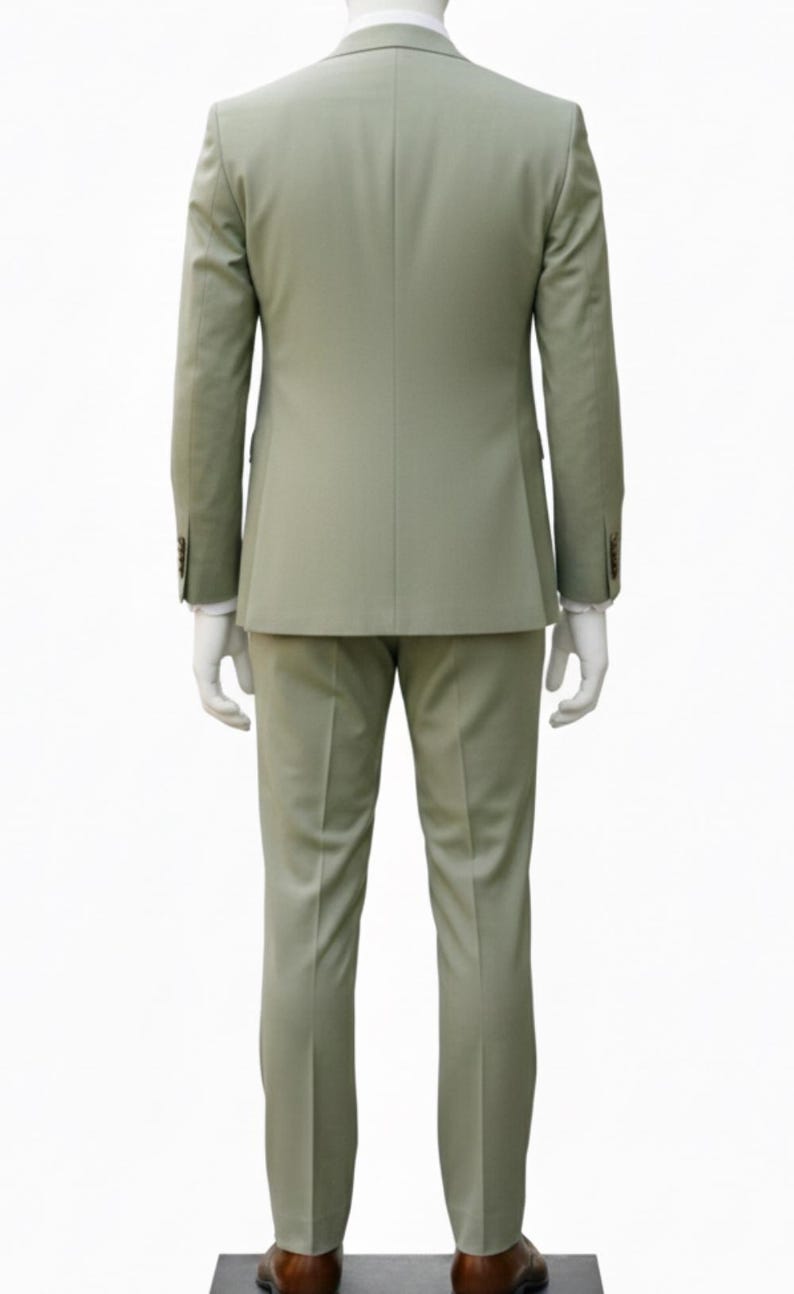 K&ouml;nnte beinhalten: Ein hellgr&uuml;ner Anzug, bestehend aus Blazer und Hose, pr&auml;sentiert auf einer Schaufensterpuppe. Der Blazer hat zwei Kn&ouml;pfe an jeder Manschette. Der Anzug ist einfarbig und scheint aus einem glatten Stoff zu sein. Braune Lederschuhe sind sichtbar.