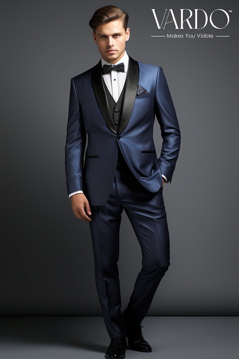 May include: A man wearing a dark blue tuxedo with a black satin lapel and a black bow tie. The tuxedo has a black satin trim on the pockets and sleeves. The man is standing on a gray background.