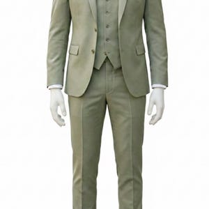 K&ouml;nnte beinhalten: Ein dreiteiliger Anzug in gedecktem Salbeigr&uuml;n, pr&auml;sentiert auf einer Schaufensterpuppe. Der Anzug besteht aus Blazer, Weste und Hose. Ein wei&szlig;es Hemd, eine gemusterte Krawatte und ein Einstecktuch setzen Akzente. Braune Lederschuhe runden das Outfit ab.