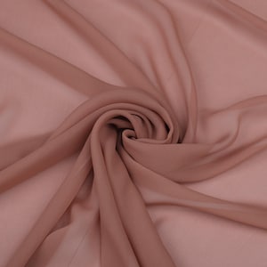 Könnte beinhalten: Nahaufnahme eines fließenden, transparenten Stoffes in einem gedämpften Rosaton. Der Stoff ist drapiert und gewirbelt, wodurch weiche Falten und Schatten entstehen. Das Material wirkt leicht und zart, ideal für Kleidung oder Dekorationsprojekte.