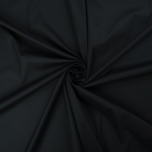 May include: A close-up of a black fabric with a smooth texture. The fabric is folded and draped, creating soft folds and curves.