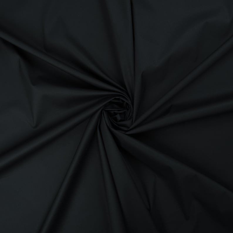 May include: A close-up of a black fabric with a smooth texture. The fabric is folded and draped, creating soft folds and curves.