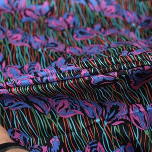 May include: Close-up of a black fabric with a colourful floral print. The fabric has a striped pattern and features pink, blue, and green flowers.
