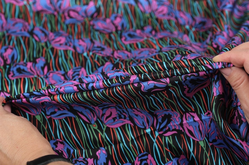 May include: Close-up of a black fabric with a colourful floral print. The fabric has a striped pattern and features pink, blue, and green flowers.
