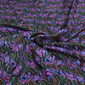 May include: Black fabric with a repeating pattern of pink and blue stylised flowers on thin black, green, and red lines.