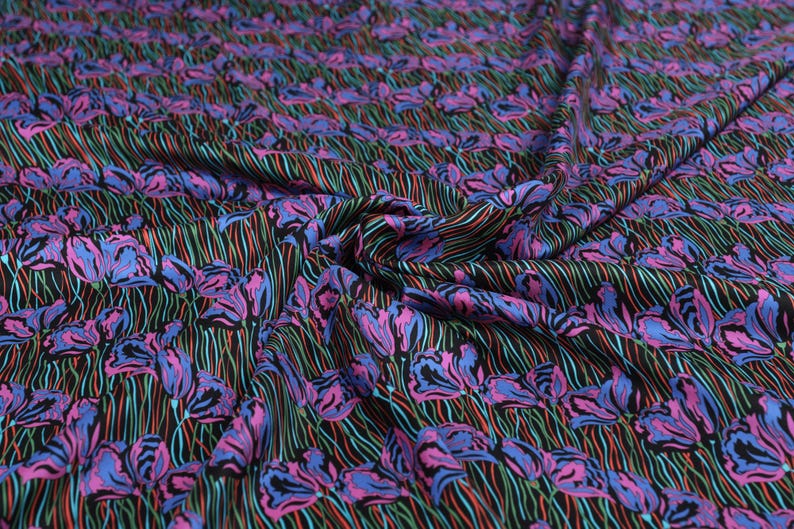 May include: Black fabric with a repeating pattern of pink and blue stylised flowers on thin black, green, and red lines.