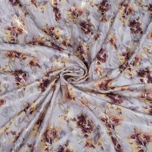 May include: A close-up of a white fabric with a gold and burgundy floral print. The fabric is soft and flowing, and the print is subtle and elegant.