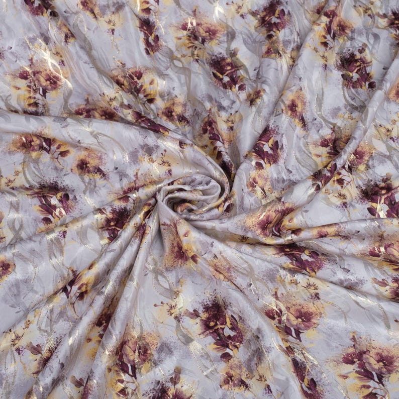 May include: A close-up of a white fabric with a gold and burgundy floral print. The fabric is soft and flowing, and the print is subtle and elegant.