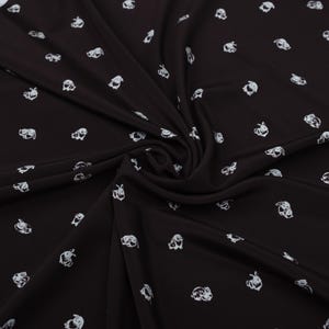 May include: Black fabric with a repeating pattern of white bunny illustrations. The fabric is draped, showing folds and shadows. The bunnies are depicted in a simple, cartoonish style, scattered across the surface.