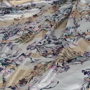 May include: White fabric with a gold and silver metallic sheen. The fabric has a floral pattern with pink, purple, and blue flowers.