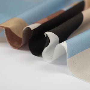 Puede incluir: Primer plano de una tela con rayas de diferentes colores, incluyendo azul, marr&oacute;n, negro y blanco. La tela tiene una superficie texturizada y est&aacute; doblada.